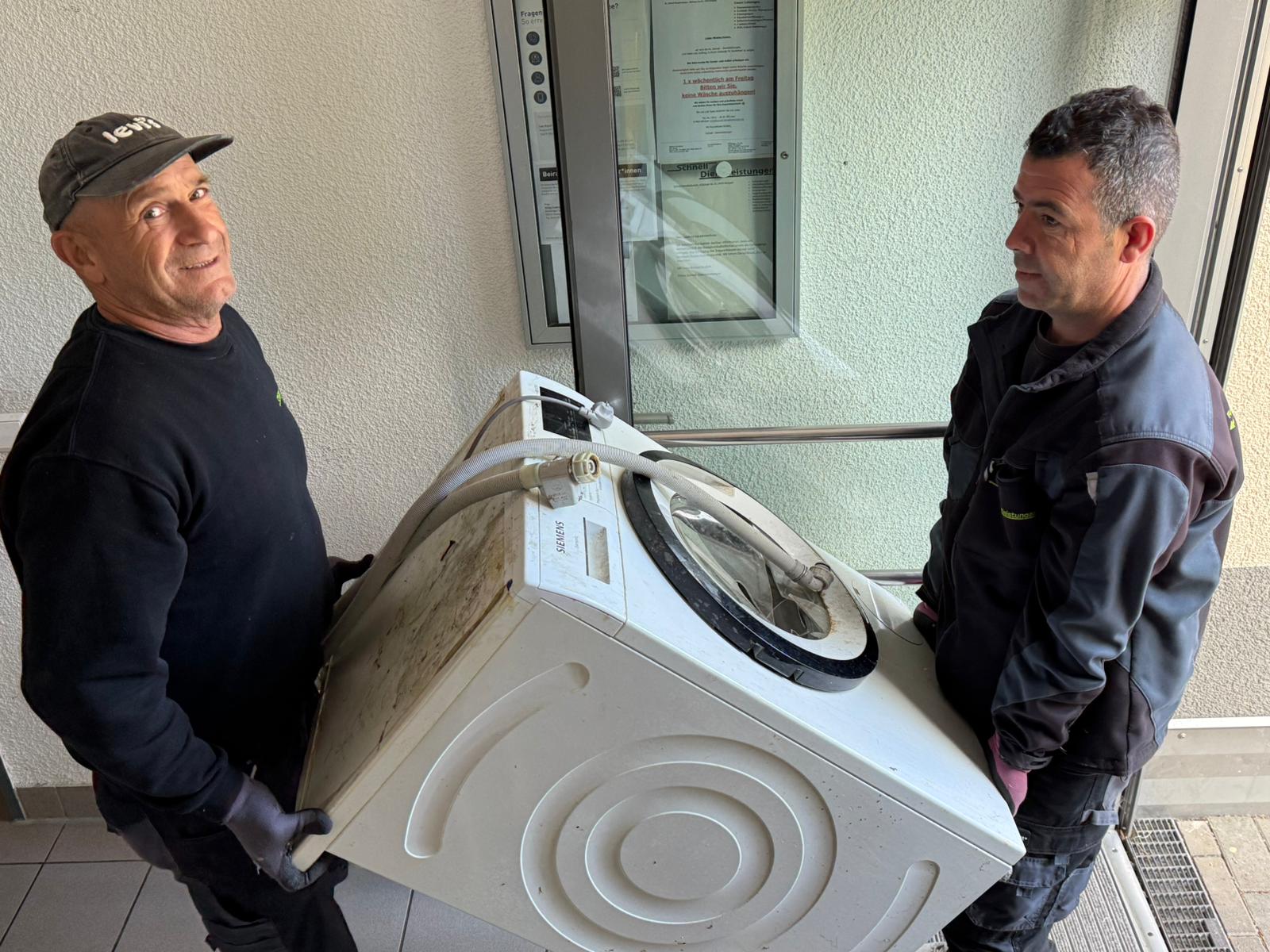 Waschmaschine entsorgen in Stuttgart Zwei Mitarbeiter tragen eine Waschmaschine aus einer Wohnung in Stuttgart – Elektroschrott Stuttgart